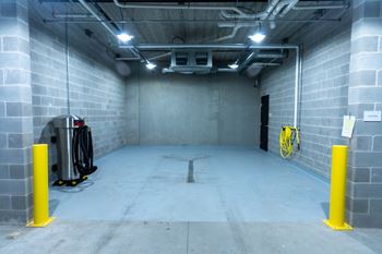 A large, empty room with a concrete floor and walls, equipped with a bike rack and a trash can.